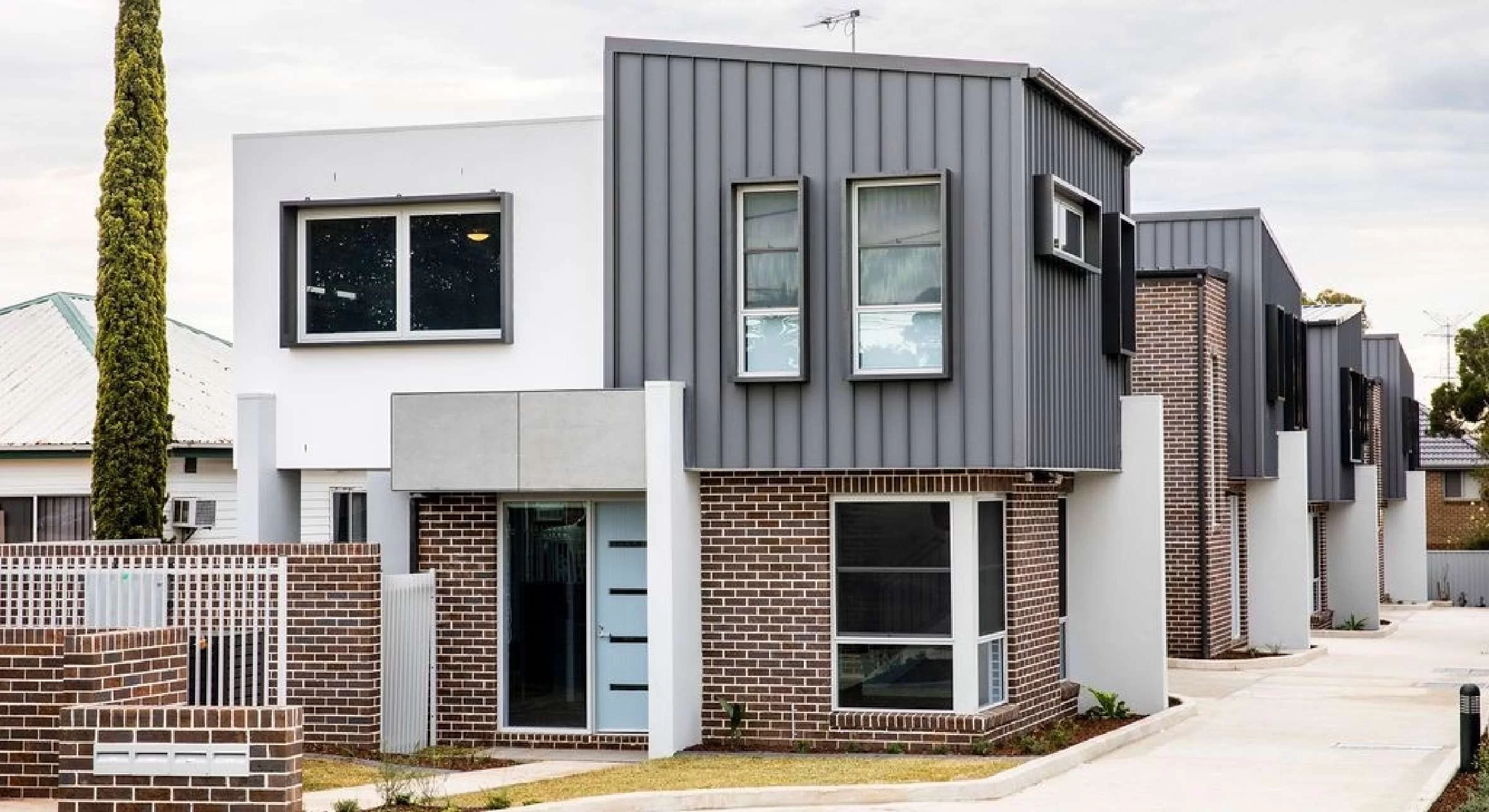 A row of contemporary townhouses featuring a mix of brick ground floors